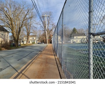 An Empty Suburban Street Along A Sidewalk With A Fence Along The Other Side.