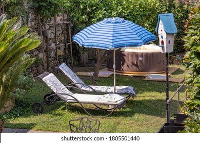 Empty Sun Loungers Under An Umbrella In A Backyard With Inflatable Pool