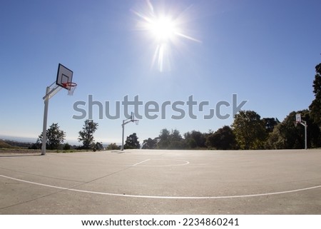Empty sunlit basketball court in city park on hot sunny day under blue zenith sky. Bright sun in the sky. Sports, lifestyle, leisure activity concept