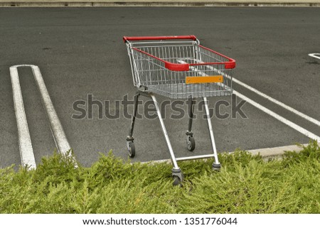 Empty supermarket shopping cart left abandoned in car park lot with wheels on grass