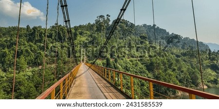Empty suspension bridge with yellow railings over a lush green forest valley, suitable for adventure travel and exploration themes with space for text