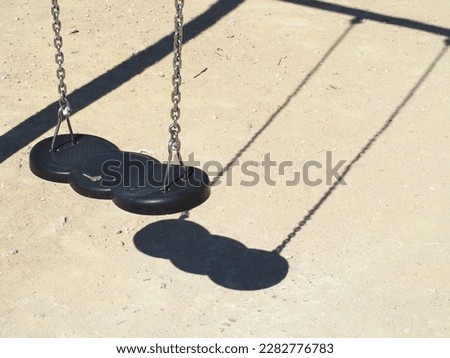 Empty swing on a bright sunny day. Shadow on the ground.