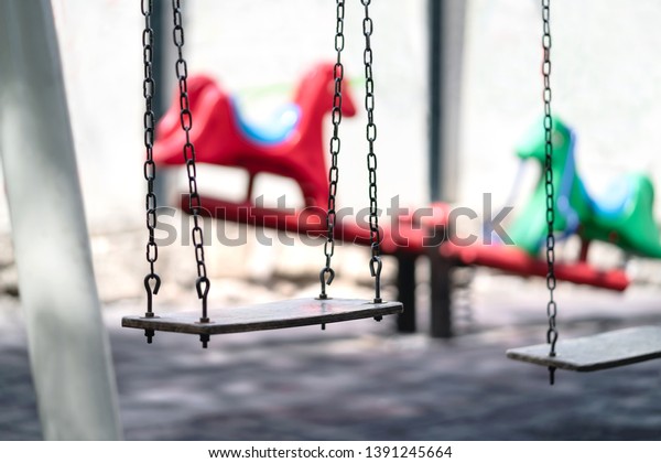 Empty swing at a playground. Sad dramatic mood for\
negative themes such as bullying at school, child abuse,\
pedophilia, traumatic childhood or kidnap. Seesaw in the\
background. Old retro vintage\
feel.