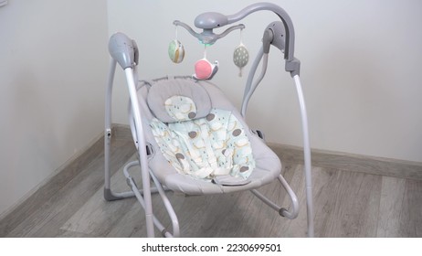 An empty swing-cradle swings in the room. Children's automatic swing for an infant. - Shutterstock ID 2230699501