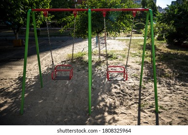 Empty Swing-set On Playground Because Of COVID Lockdown. Sand Underneath The Swings And A Grassy Area, Then Many Trees Behind. Good Summer Camp Image.