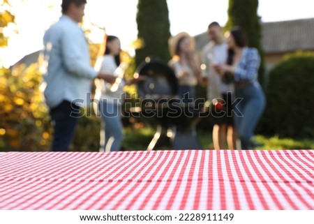 Empty table and blurred view of friends having barbecue party outdoors. Space for text