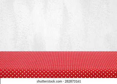 Empty table covered with red polka dot tablecloth over white cement wall background, for product display montage