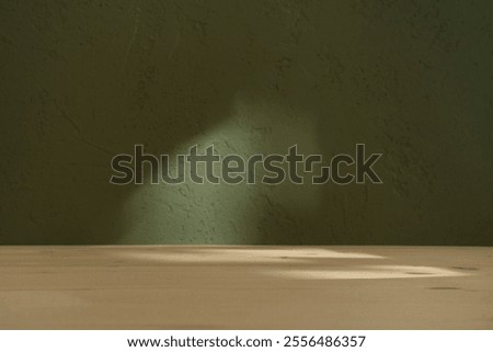 Empty table and darkgreen wall. Table with sun reflections and leaves shadows on khaki green wall. Background with bokeh for product presentation. Mock up for branding products, cosmetics food.