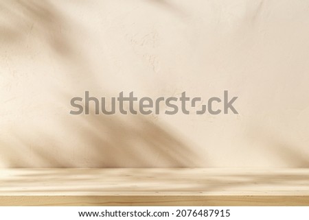 Empty table on beige texture wall background. Composition with monstera leaves shadow on the wall. Mock up for presentation, branding products, cosmetics food or jewellery.