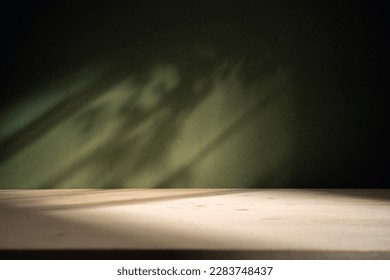 Empty table on dark green texture wall background. Composition with monstera leaves shadow on the wall and light reflections. Mock up for presentation, branding products, cosmetics food or jewelry.