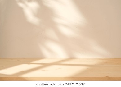 Empty table on white wall background with leaves and window frame shadow on the wall and wooden desk. Mock up for presentation, branding products, cosmetics, food or jewelry.