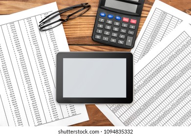 Empty tablet PC with financial documents and calculator on the table.
