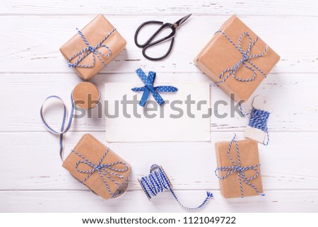 Empty tag and wrapped  gift boxes with presents, scissors and  blue ribbon on textured wooden background. Selective focus is on tag. Place for text. Flat lay.