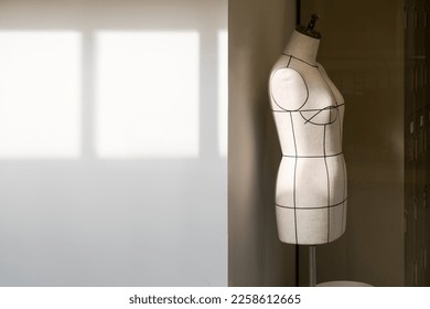 Empty tailor's textile female mannequin with black lines with sunlight on it for dressmaker working and designing new fashion collections with patterns and draping in an atelier tailor workshop. - Shutterstock ID 2258612665