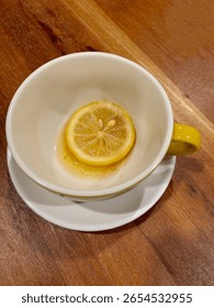 An empty tea cup with a slice of lemon and some leftover tea, on a wooden table.