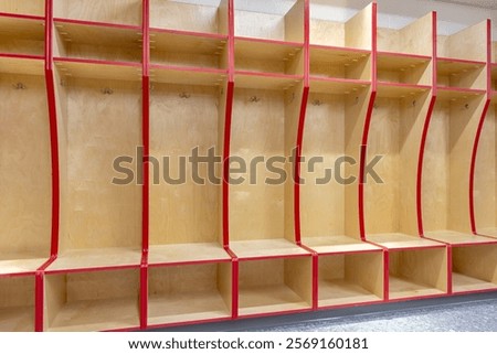 Empty team locker, changing room with traditional open wooden lockers with a red trim.
