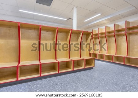 Empty team locker, changing room with traditional open wooden lockers with a red trim.