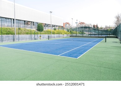 An empty tennis court with a blue and green surface, located in a large sports complex. Concept of tennis facility and preparation for sports. - Powered by Shutterstock