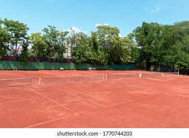 Empty Tennis Court On Sunny Summer Day. View From Above Of A Red Clay Tennis Court, Green Trees And A Blue Sky In The Background. Outdoor Sports Playground For Tennis. Copy Space For Text Or Design