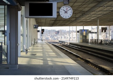 Empty train station platform with a clock and empty message board on a sunny day with a slightly blurred background