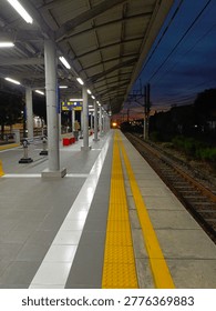 Empty train station platform at dusk with leading lines and yellow tactile paving, railway tracks stretching into the distance, urban transportation concept.