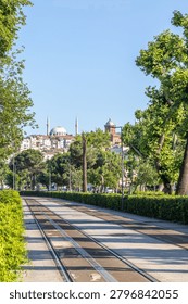 Empty tramway tracks running through a lush green public park under a clear blue sky. Modern urban public transit infrastructure and sustainable transportation concept.