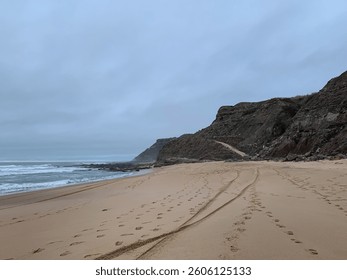 Empty tranquil beach with rocky cliffs under overcast sky, capturing serene coastal landscape, perfect for summer getaways or relaxation