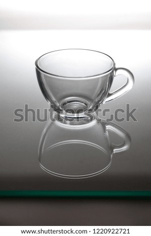 Empty transparent glass tea cup stands on the glass closeup. The reflection is visible below.
