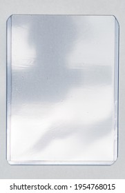 Empty Transparent Plastic Card Top Loader Case On White Paper Background, Gaming Or Trading Card Placeholder With Nice Light Reflection.