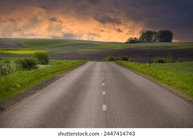 Empty two lane asphalt road running through a serene and open countryside landscape. Surrounding the road are grassy plains and small hills