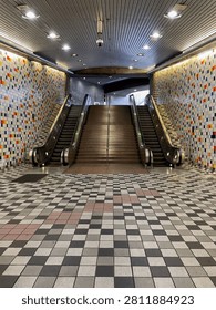 Empty underground subway station with escalators, central stairs, and colorful mosaic tile walls
