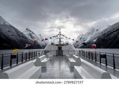 An empty upper deck of a tour ferry in fjords with nautical flags blowing in the wind. Winter scenery in Geirangerfjord, Sunnmore region, Norway.