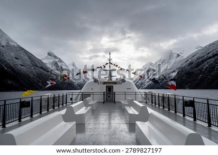 An empty upper deck of a tour ferry in fjords with nautical flags blowing in the wind. Winter scenery in Geirangerfjord, Sunnmore region, Norway.