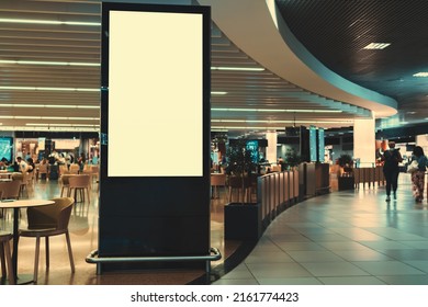An empty vertical advertising banner mockup in front of a crowded shopping mall or an airport food court with tables and customers in the background and a copy space place on the right for an ad text - Shutterstock ID 2161774423