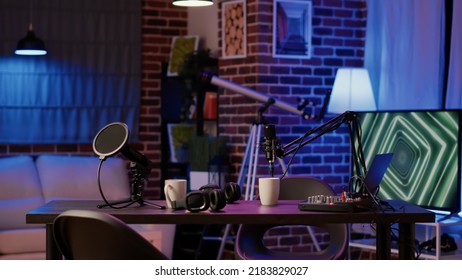 Empty vlogger desk with professional streaming equipment to broadcast live talk show on social media. Cozy ambient room with podcast station, microphone and headphones, sound production. - Powered by Shutterstock