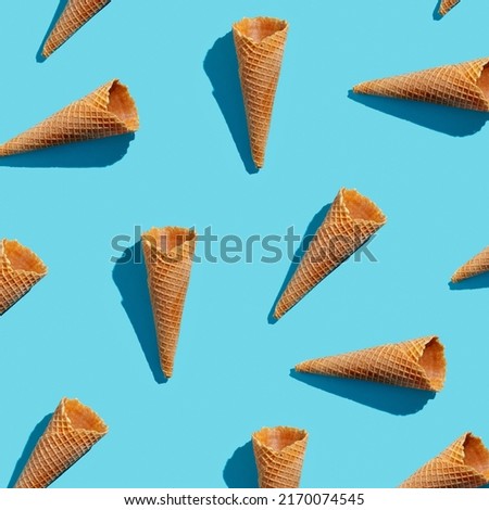 Empty wafer ice cream cones continuous pattern on blue background  top view, hard light