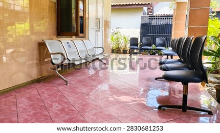 An empty waiting area featuring two rows of chairs, one made of metal and the other upholstered in dark fabric, set on a glossy tiled floor. The space appears quiet and ready for visitors.