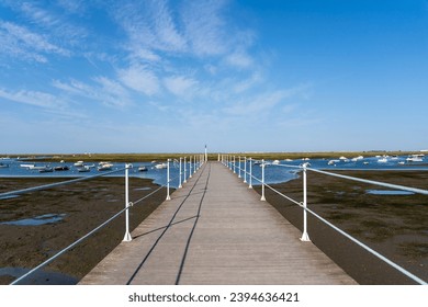 Empty walkway over blue ocean, coastline and horizon seen a large long wooden jetty with a thin white metal railing along the edges but in the perspective distance a blue sky and an ocean with boats - Powered by Shutterstock