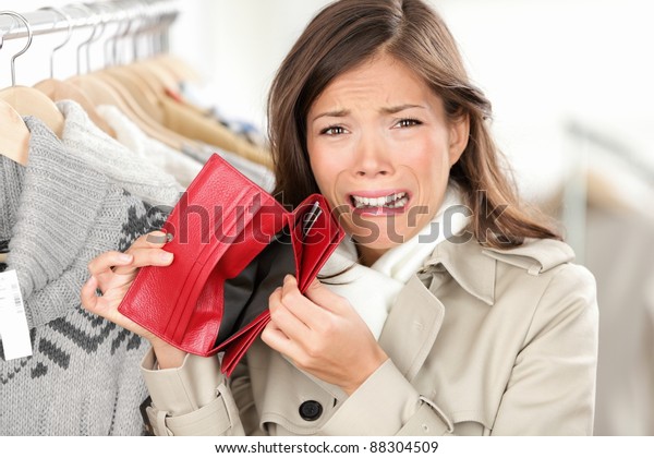 「空の財布 財布の買い物にお金を持たない女性。服屋の女性の買い物客は、お金がなくて泣いて怒っている。白人とアジア人の女性が混ざった人種の