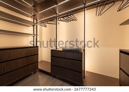 Empty wardrobe with backlit illuminations. Empty corner closet with bunch of black hangers.