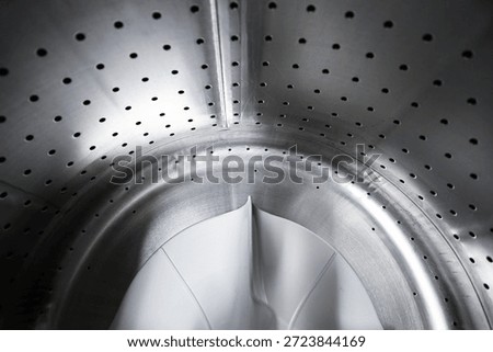 Empty washing machine drum interior closeup. Stainless steel perforated surface and plastic paddle inside modern washer. Clean appliance detail before laundry cycle at home. Household hygiene concept.