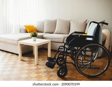 Empty wheelchair in the livingroom. Lonely and healthcare concept. Empty wheelchair dor a disable person with blue plaid on background of big couch with cushions in living-room - Powered by Shutterstock