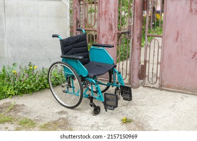 Empty Wheelchair Parked Near The House.