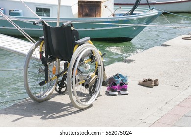 Empty wheelchair and shoes on the beach near the sea with boats  - Shutterstock ID 562075024