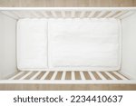 Empty white baby crib with mattress, sheet, pillow and blanket. Closeup. Top view.