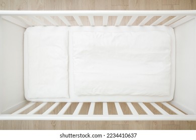 Empty white baby crib with mattress, sheet, pillow and blanket. Closeup. Top view.