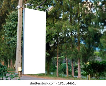 Empty White Blank Banner On Electric Pole For Advertising Beside The Road Near The Tree And Green Garden. Billboard Mockup Or Flag Street Hanging On The Concrete Pole.