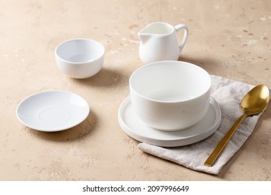 Empty white bowl, white plates, gold spoon and linen napkin on beige table. Shop tablewere concept