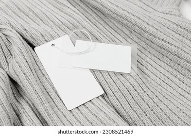 Empty white cardboard tag with string on grey sweater. Label blank mockup on a clothes, to place your design.  Price tag, sale, address label. Shopping concept. 