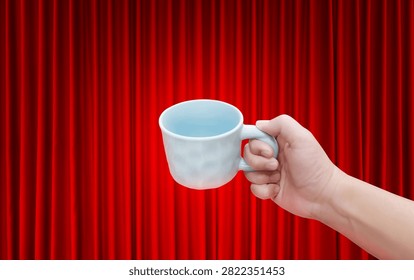 An empty white ceramic coffee cup is in a man's hand, with a red curtain as a background.